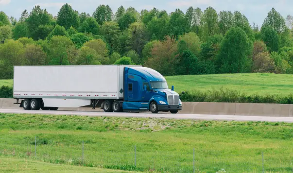 A semi truck driving down the road near some trees.